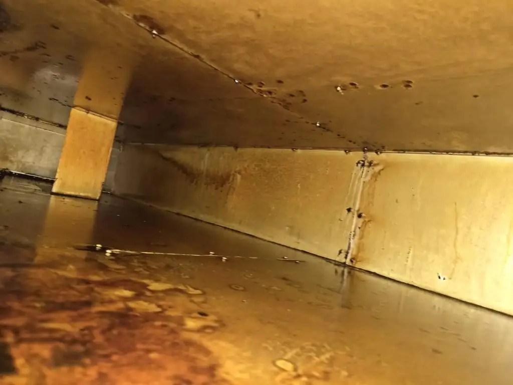 Binnenzijde van een rechthoekig metalen vetkanaal met vetafzetting op de bodem, de wanden en rond een steun.